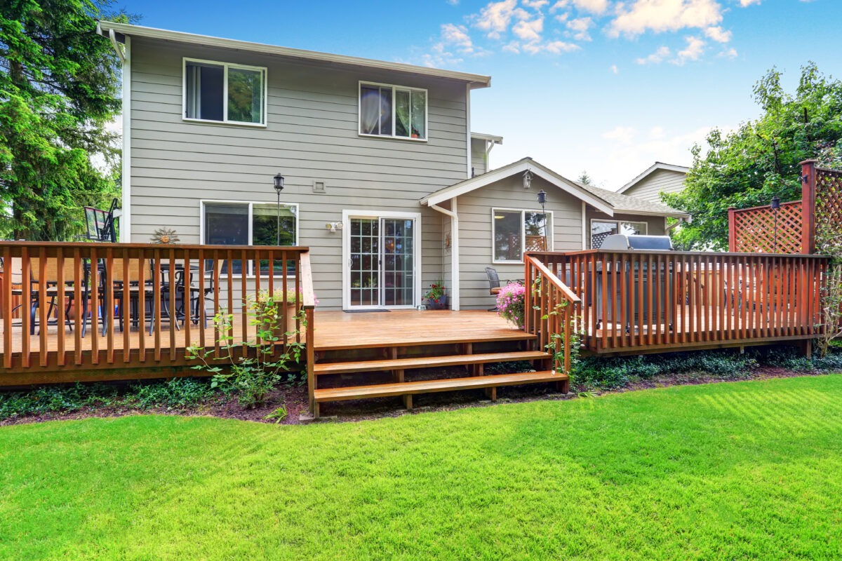 Back yard house exterior with spacious wooden deck with patio area and attached pergola displaying high quality types of deck material