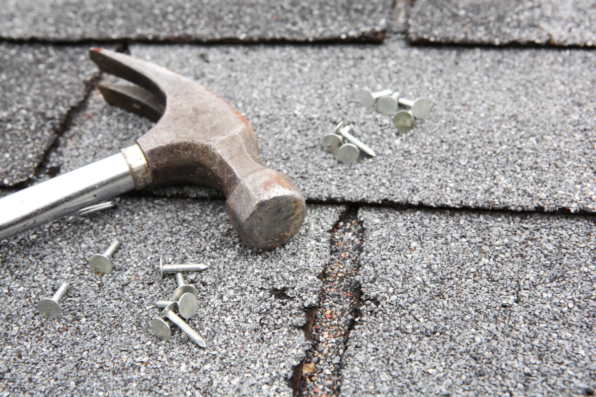 close up view of an old roof with asphalt shingles , nails, and a hammer