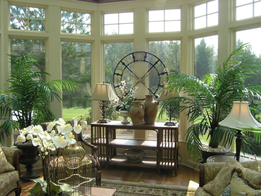 view is looking towards window of a 12x12 sunroom with plants in front and a nice table with a lamp on it