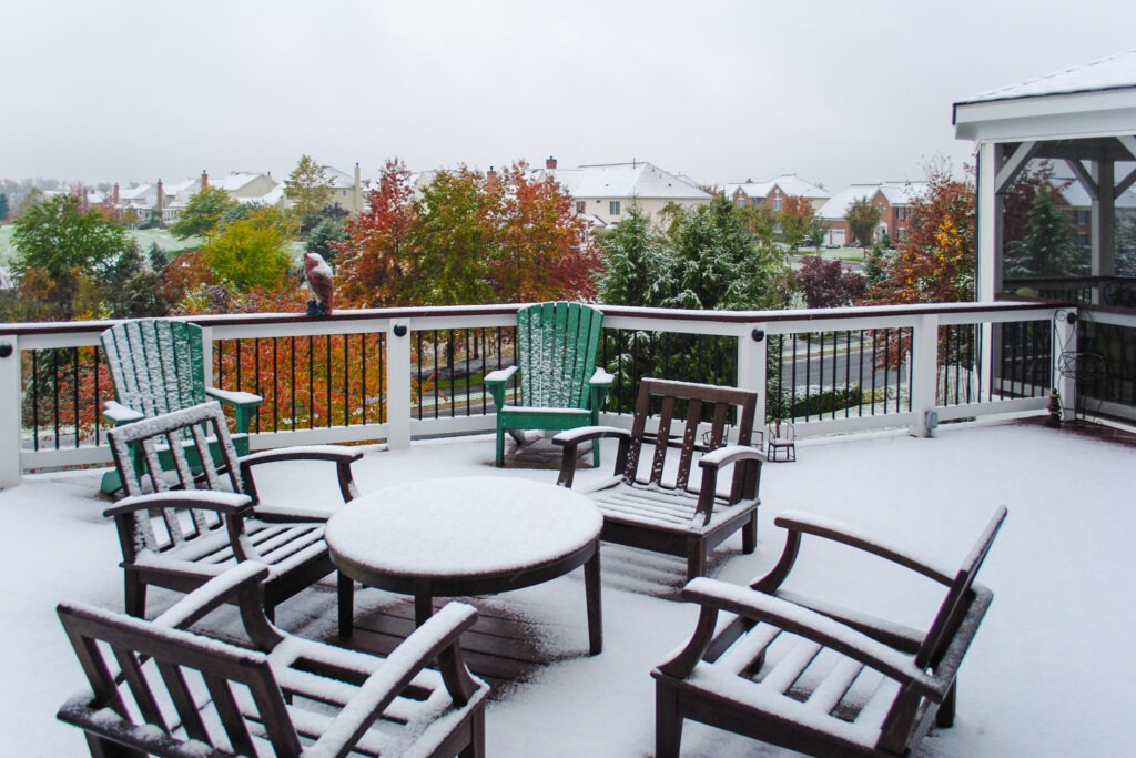 deck furniture covered in early fall snowfall. porch ready for winter. chairs and a table covered in snow. snowstorm in autumn
