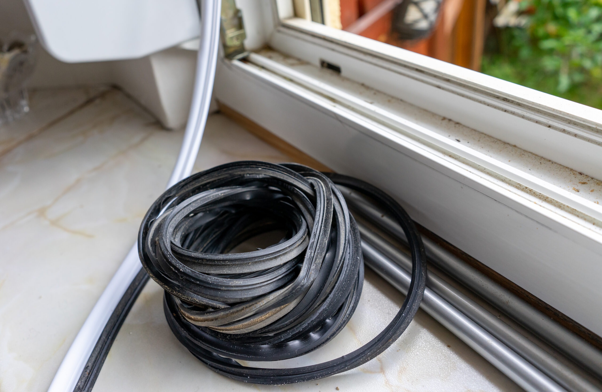 roll of black window seal sitting next to a window to fix a leaking window letting cold air in